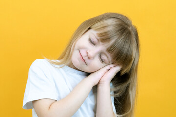 cute smiling sleepy calm girl with closed eyes folded her palms under her head. dreaming on yellow background close up