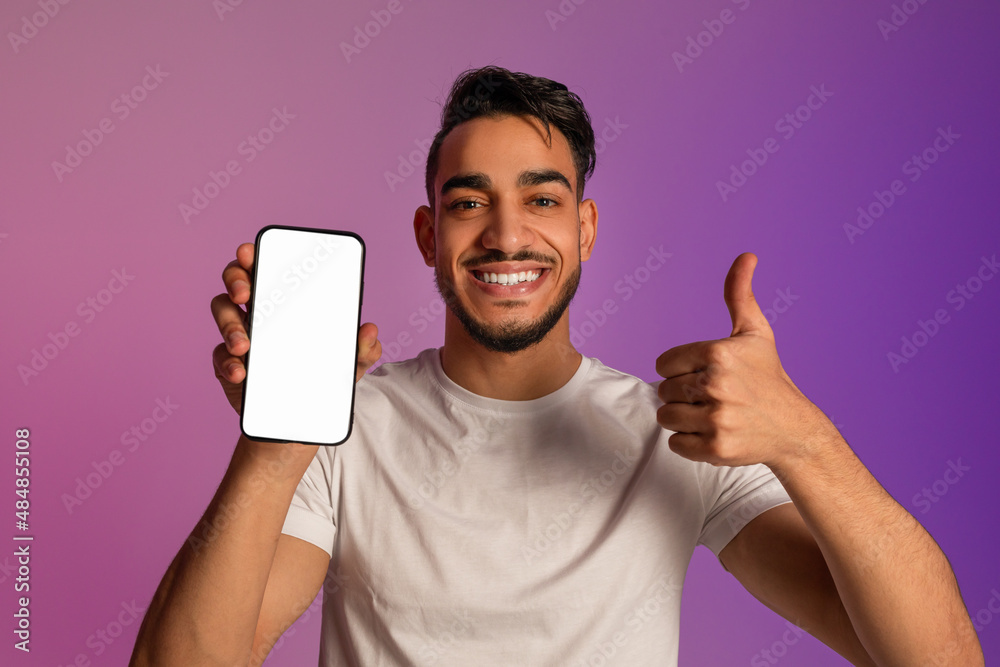 Poster happy arab man showing thumb up gesture, demonstrating smartphone with empty screen in neon light, m
