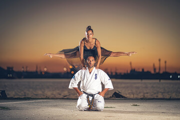 Girl gymnast making a jump over a karate man at sunset