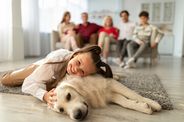 Adorable little girl lying on floor with golden retriever dog, hugging and cuddling with pet at home. Family times