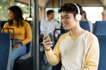 Happy Asian guy using smartphone and headphones in bus © Prostock-studio