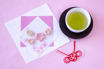 和紙の上の桜の干菓子と紅白の水引飾りと緑茶