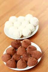 Chocolates made from dark chocolate. White round coconut flakes on the table.