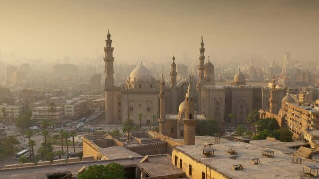 Zoom out of Mosque of Sultan Hassan, Cairo, Egypt at sunset. Cairo city in light fog in the rays of setting sun