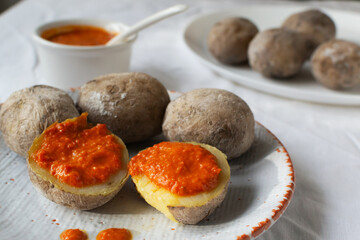 Potatoes on a white plate with red sauce on a white tablecloth. A traditional Canarian dish is papas arrugadas. Vegetables are boiled in water with a lot of salt.