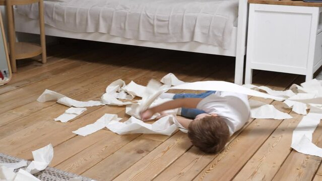 Small child has made a mess, scattered toilet paper around the apartment and happily plays. Little child having fun in the midst of chaos