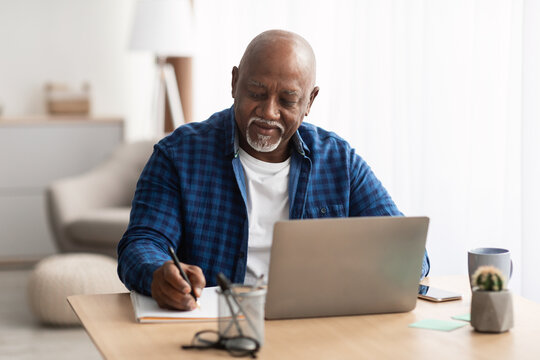 Senior Black Man At Laptop Taking Notes Indoors