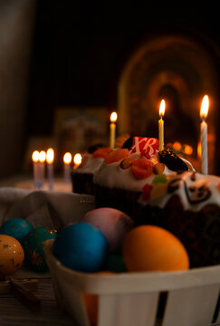 Easter still life with Easter cake and eggs in the basket, burning candles in the darkness of monastry church with Russian icons in the background, close up