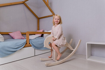 little blonde girl is swinging having fun and playing. A child swings on a wooden horse. The baby...