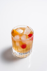 Vaso de vermut con hielo decorado con cerezas y rodajas de naranja sobre mesa blanca	