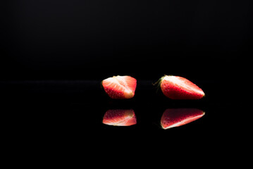 Una fresa cortada a la mitad aislada . Reflejo espejo sobre agua y fondo negro