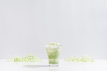 Un vaso de té verde matcha con leche decorado con flores sobre una mesa blanca y fondo gris claro