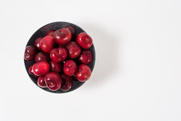 Cerezas dulces rojas en un bol sobre fondo blanco. Vista superior