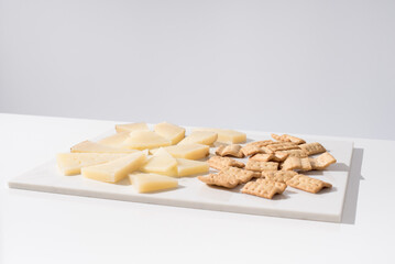 Trozos de queso manchego de oveja curado con tostadas de pan crujiente sobre una mesa blanca. Tapas españolas	
