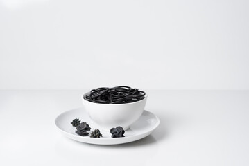 Espaguetis negros de tinta de sepia en un plato blanco  sobre fondo blanco	