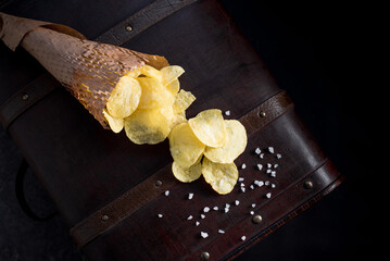 Patatas fritas saladas en un cono de papel. Aperitivo sobre fondo oscuro. Vista superior