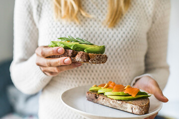 Close up of woman holding plate with avocado toast as fresh snack, day light. 