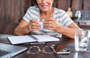 Elderly woman sit at table with wireless earphones take part in educational webinar using laptop. Closeup wireless earphones. Video call event concept.