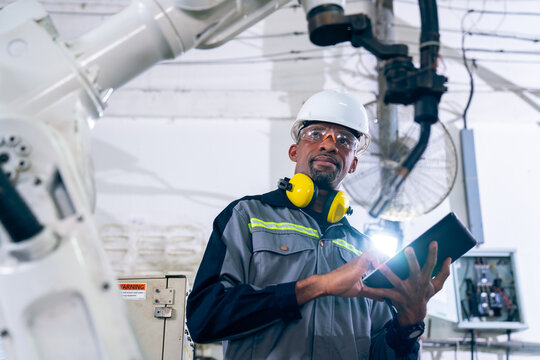 African American factory worker working with adept robotic arm in a workshop . Industry robot programming software for automated manufacturing technology .