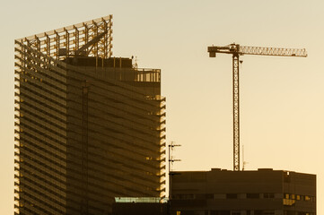 Silueta de grua, edificio moderno vanguardista y estructuras metálicas en el atardecer.