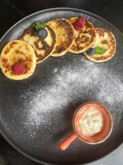 Cheese pancakes, cheesecakes in frying pan on black background with copy space. Top view, flat lay