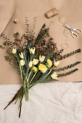 Spring flowers, bunch of yellow tulips and on beige background, craft paper, scissors and ribbon, flat lay