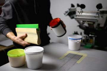 Cropped shot of artisan holding squeegee and plastisol ink near screen printing machine 
