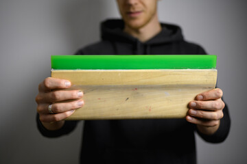 Wooden squeegee  in hands of blurred craftsman isolated on grey 