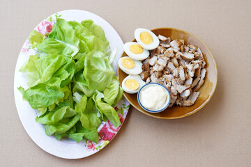 Top view of sliced grilled pork, boiled eggs and mayonnaise food and vegetables on dishes. Brown background. Concept : Healthy menu for body weight control. Eat well and healthy.  
