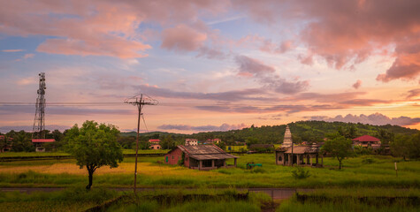 Traditional Indian village house and temple surrounded by green grass and beautiful sunset view