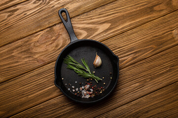Black cast iron frying pan skillet with food cooking ingredients fresh rosemary, garlic, salt and...
