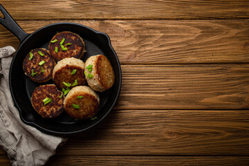 Homemade cutlets from fish, chicken or meat on black cast iron frying pan skillet on rustic wooden table, traditional meal roasted healthy cutlets in pan from above 