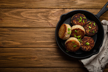 Homemade cutlets from fish, chicken or meat on black cast iron frying pan skillet on rustic wooden table, traditional meal roasted healthy cutlets in pan from above 