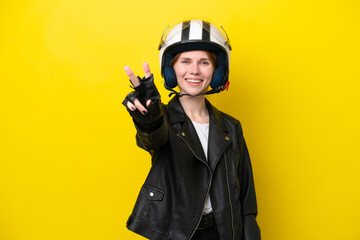 Young English woman with a motorcycle helmet isolated on yellow background smiling and showing victory sign