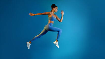Plakat Determined Young Sportswoman Jumping Posing In Mid-Air On Blue Background