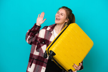 Young English woman isolated on blue background in vacation with travel suitcase and saluting