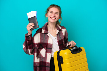 Young English woman isolated on blue background in vacation with suitcase and passport