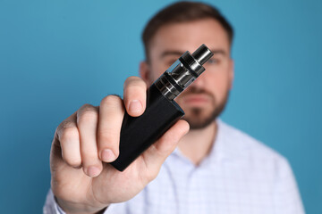 Man holding electronic cigarette against light blue background, focus on hand