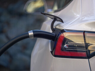 Electric car charging at charging station outdoors, closeup on power plug cord connected to charging port.