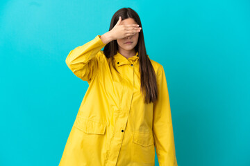 Teenager Brazilian girl wearing a rainproof coat over isolated blue background covering eyes by hands. Do not want to see something