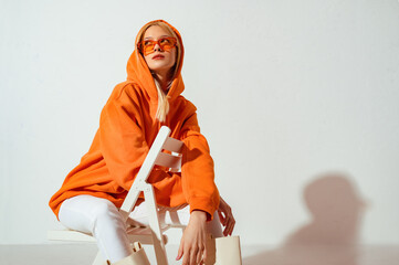 Fashionable girl wearing orange hoodie, glasses looking up,  posing on white background. Copy, empty space for text - 484876125