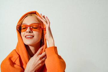 Happy smiling fashionable woman wearing orange color sunglasses, hoodie posing on white background....