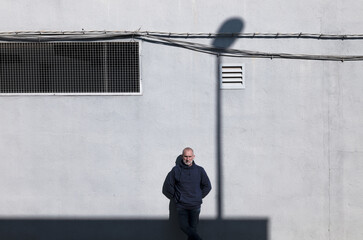 Adult man standing against white wall with shadow of street lamp