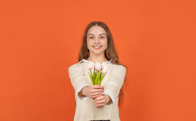 happy kid hold flowers for spring holiday. teen girl with bouquet on orange background.