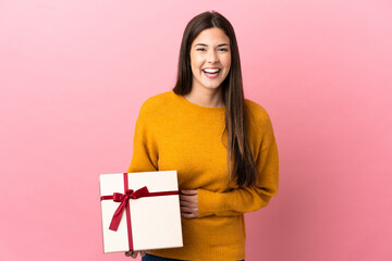 Teenager Brazilian girl holding a gift over isolated pink background smiling a lot