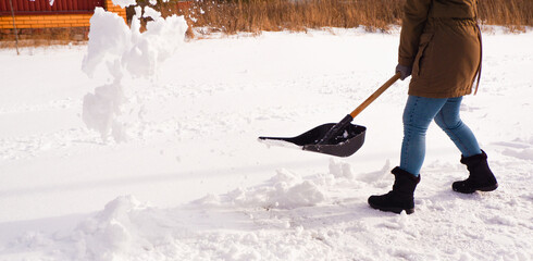 Snow removal in winter. A woman cleans the snow with a shovel in the local area. Woman clearing...