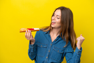 Young caucasian woman holding sashimi isolated on yellow background celebrating a victory