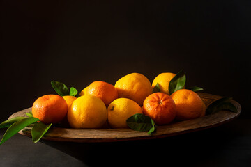 Wooden bowl of citrus fruit, oranges and mandarines, on a textured black background side lit with copy space.