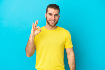 Young handsome caucasian man isolated on blue background showing ok sign with fingers