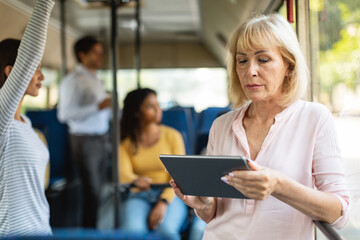 Portrait of senior woman taking bus using tablet